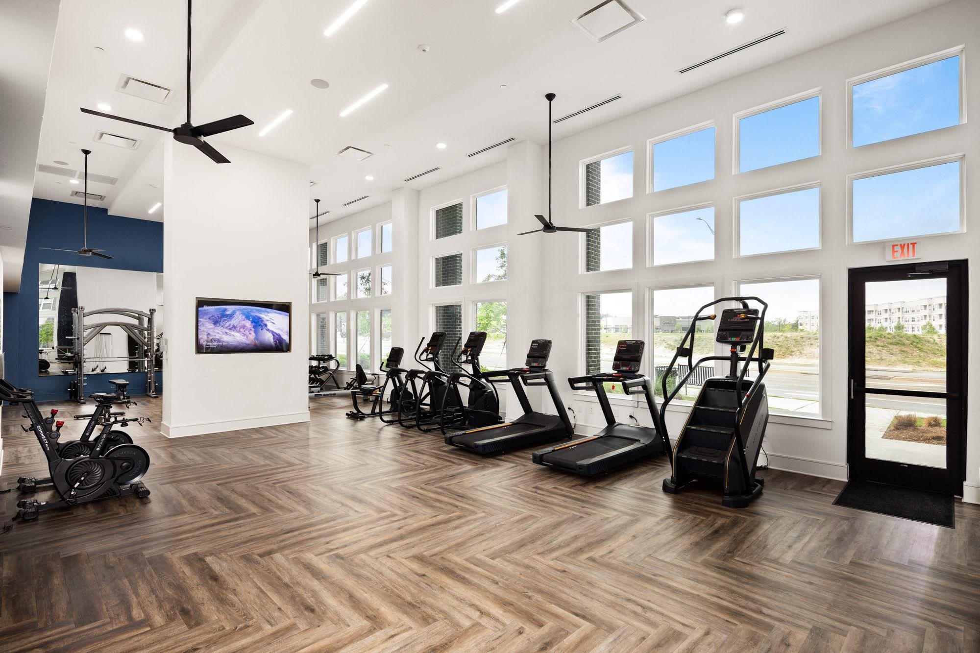 a gym with cardio equipment and large windows